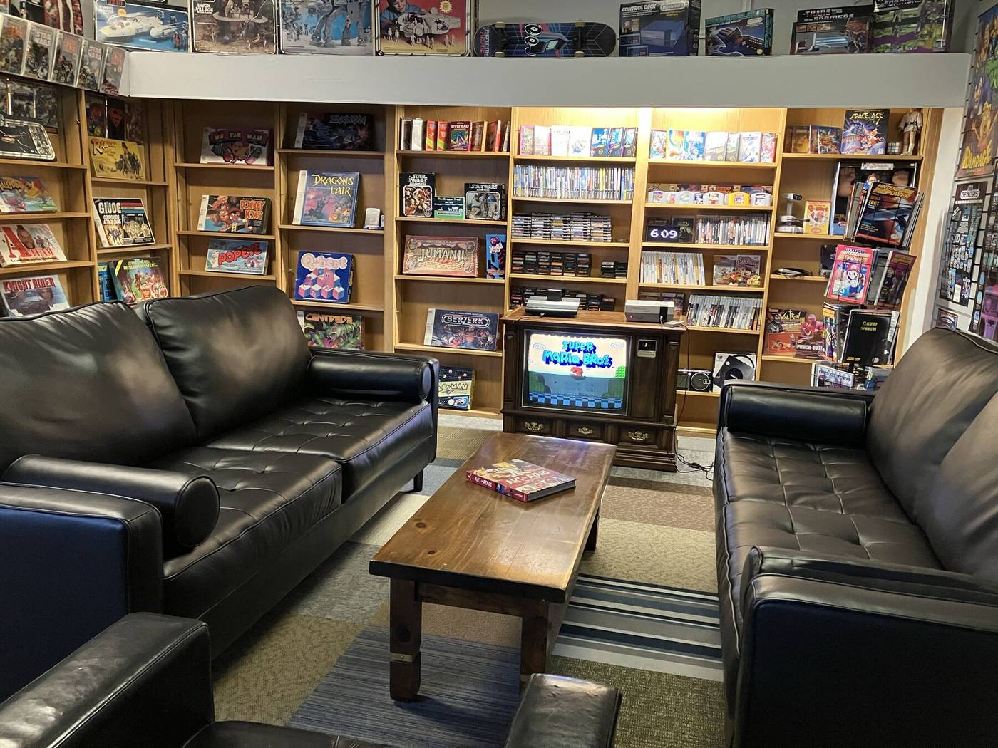Leather couches facing a vintage TV, surrounded by shelves of games
