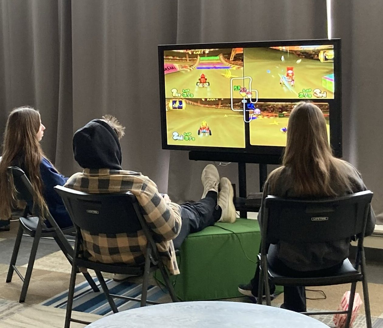 Friends playing Mario Kart on a big screen in the lounge