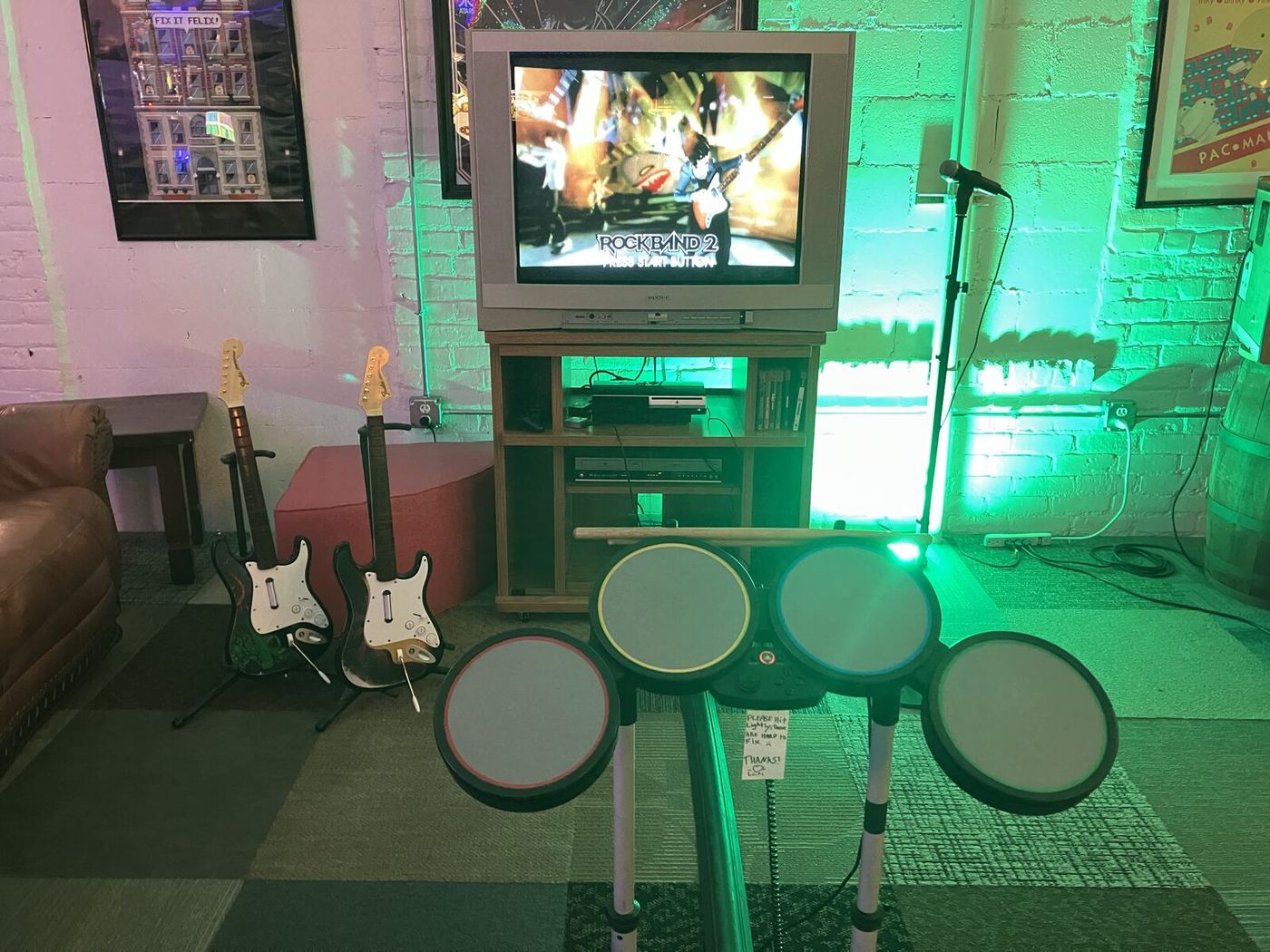 Rock Band 2 setup with two guitars, a drum kit and a microphone in front of a CRT TV